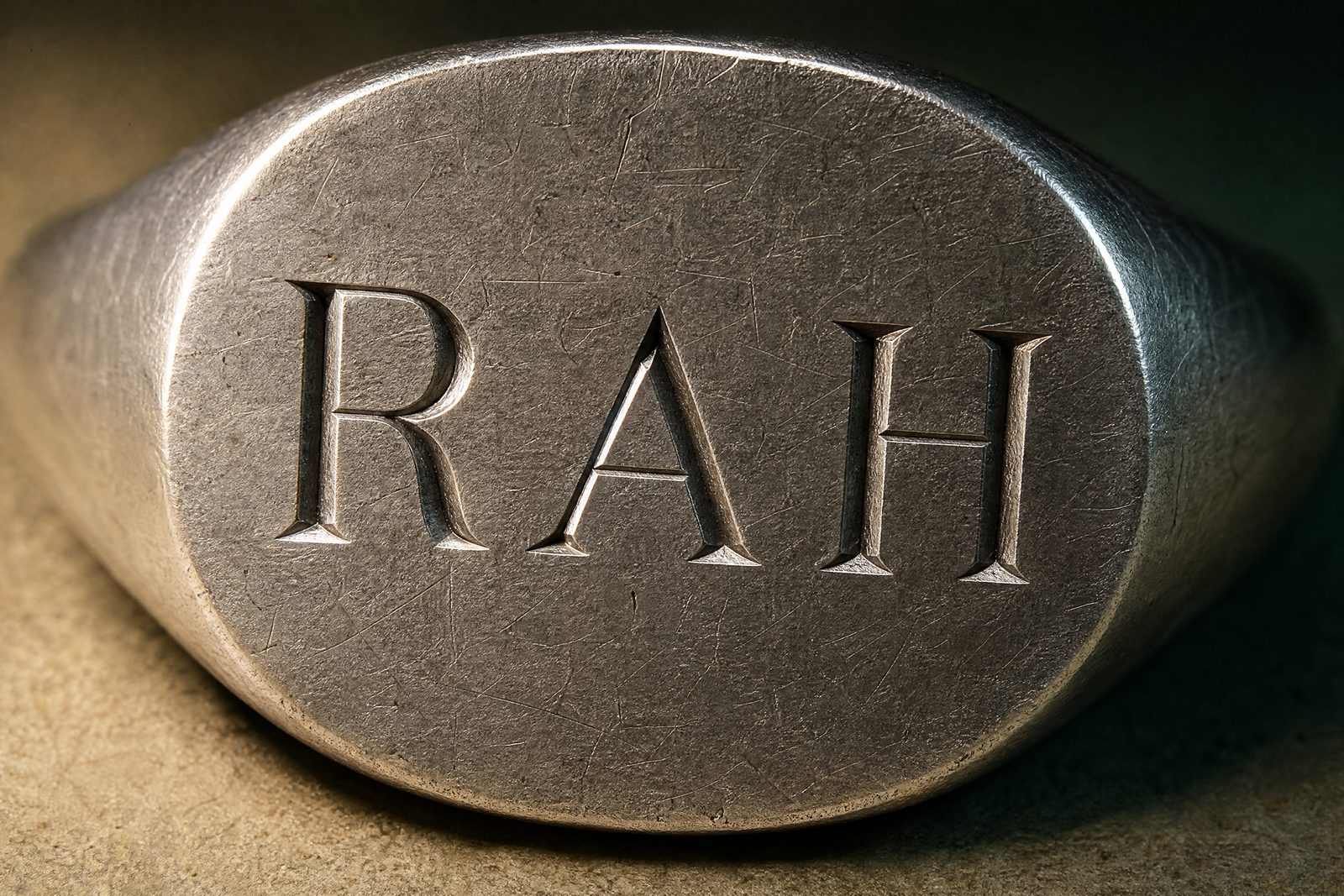 The flat oval face of a silver signet ring engraved with three plain block capital initials and nothing else.